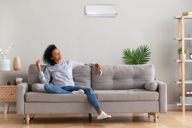Woman in living room with ductless system mounted above couch.